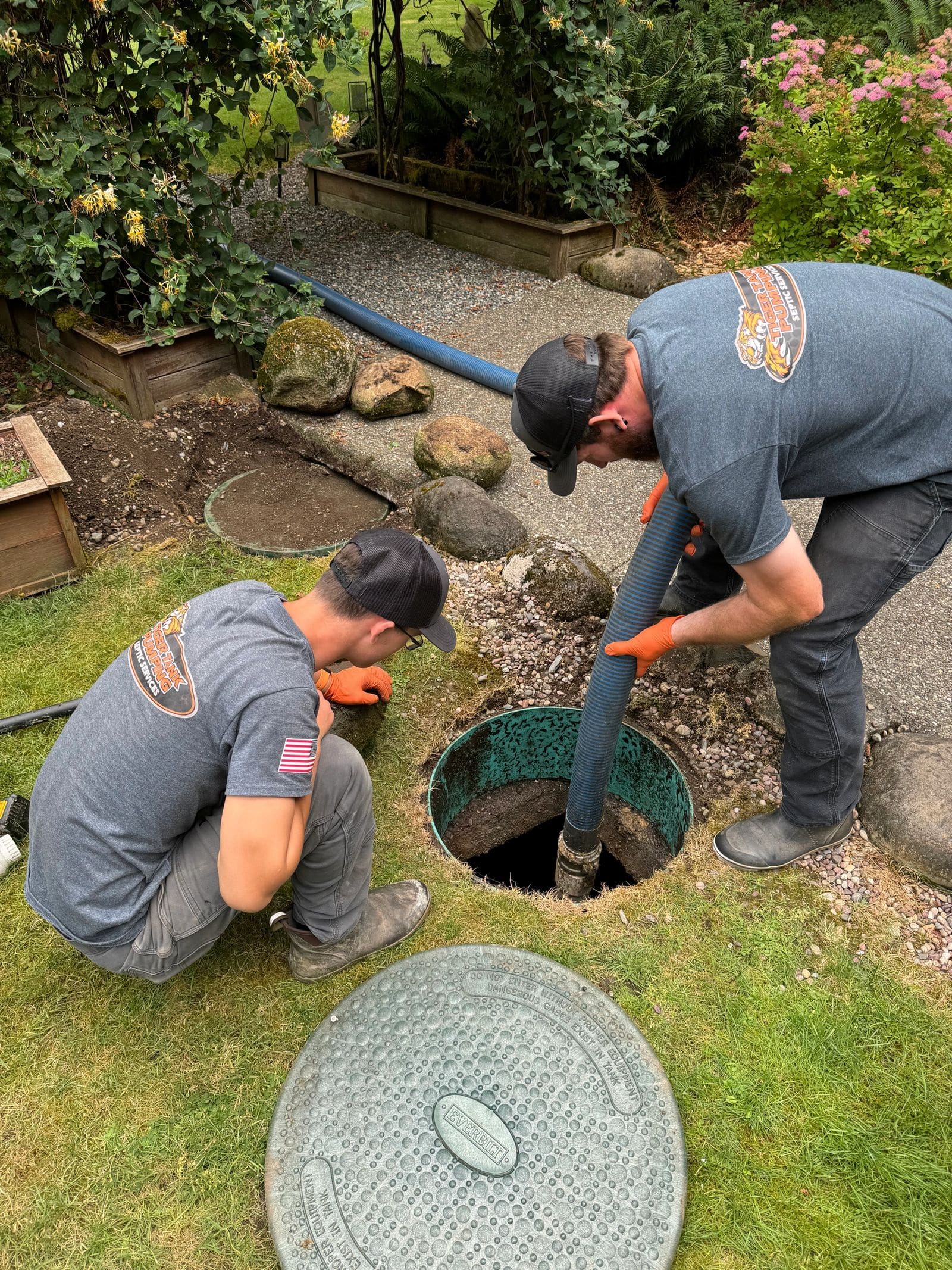 Tiger Tank Pumping technicians working at an open septic riser in a landscaped yard.